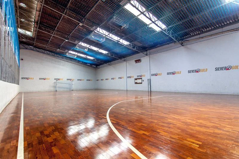 Quadra coberta de futsal com piso de tacos e rede de proteção azul no teto